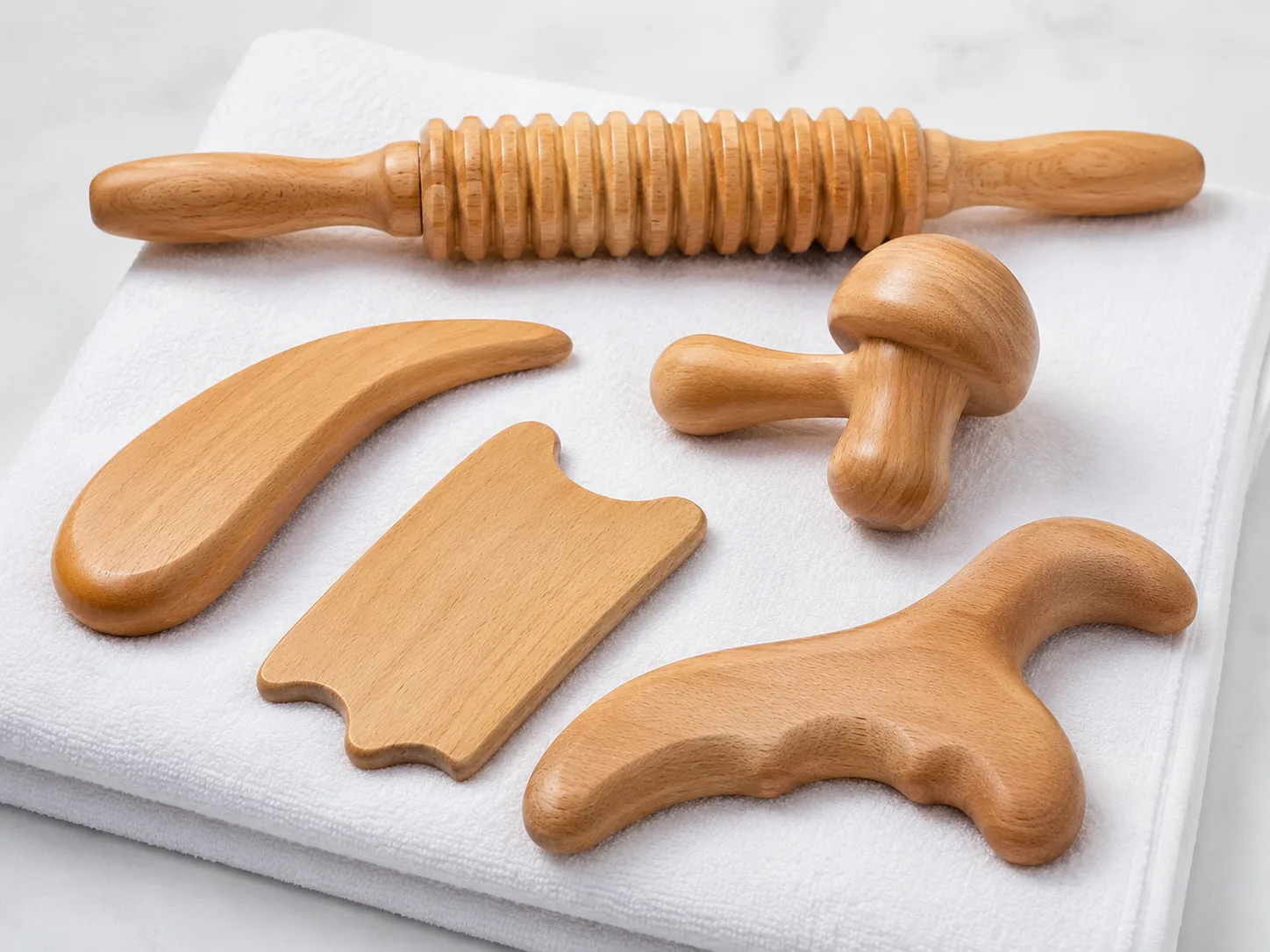 A set of purpose-made wooden manual massage tools used in Brazilian lymphatic drainage massage, laid out on a folded white towel.